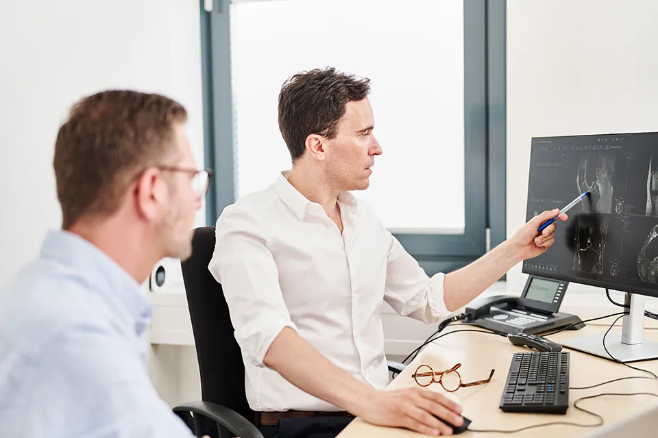 Prof. Florian Streitparth bespricht mit einem Kollegen die medizinische Bildgebung auf einem Monitor.